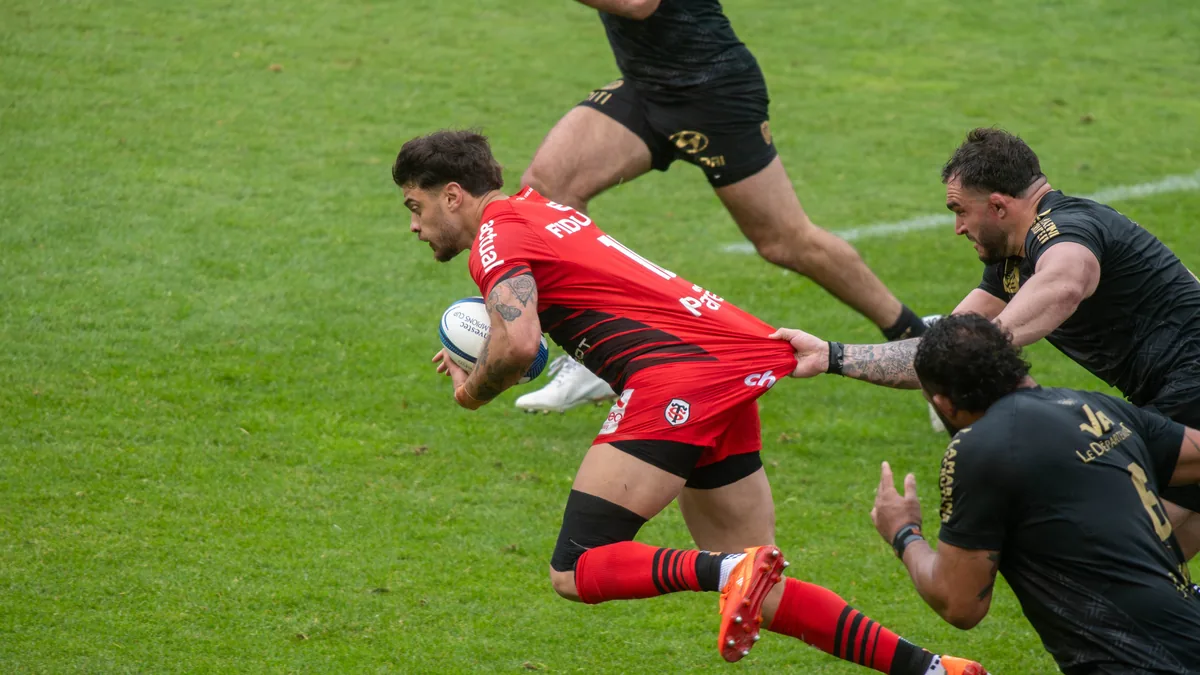 Romain Ntamack, ballon en main, retenu par le maillot par un Toulonnais, avec le Stade Toulousain à Toulon en avril 2025
