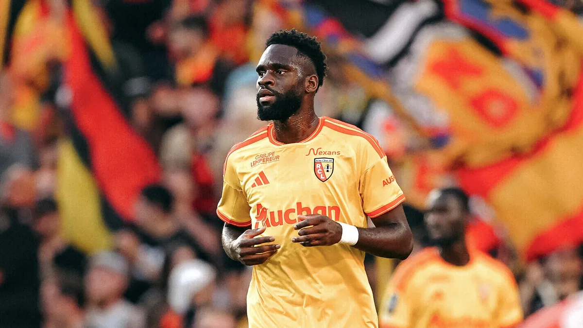 Odsonne Édouard sous le maillot jaune du RC Lens, devant les drapeaux des supporters à Bollaert