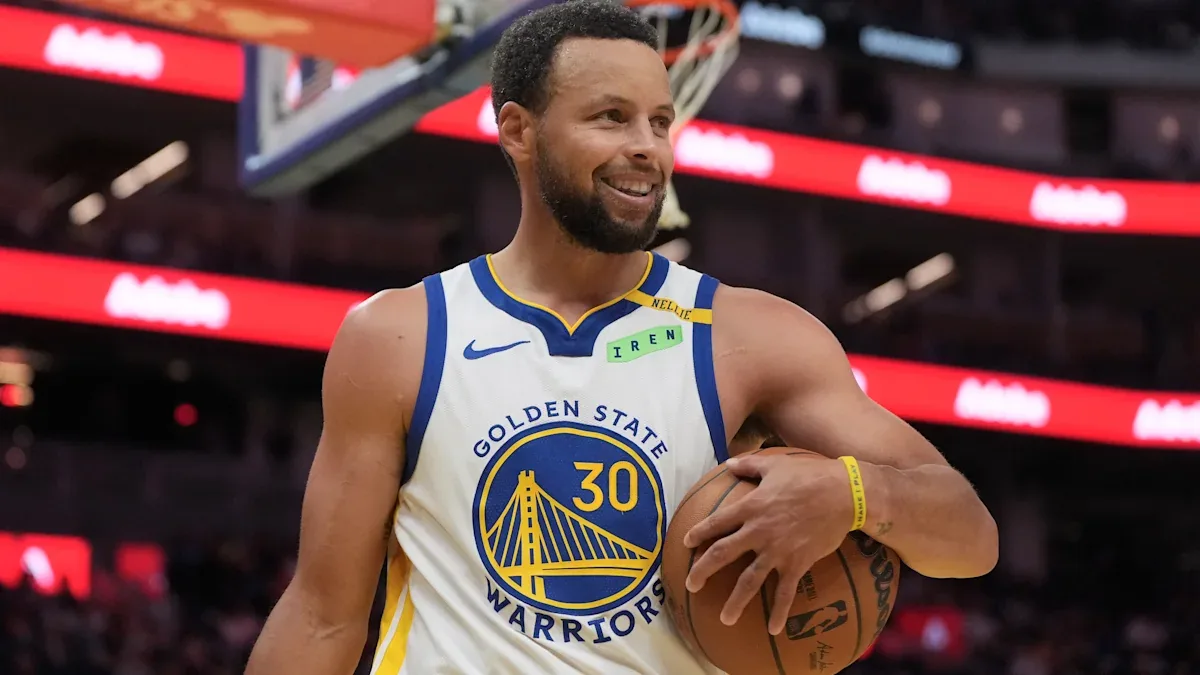 Stephen Curry souriant, ballon en main, sous le maillot des Golden State Warriors au Chase Center