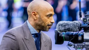 Thierry Henry en costume au bord d'un terrain face à une caméra de télévision, mai 2026